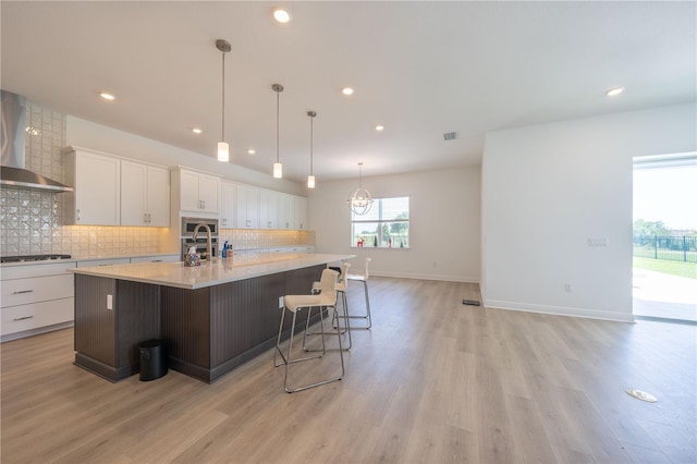 15600 Vetta Dr, Bella Collina, FL 34756 - kitchen with wall chimney range hood, decorative backsplash, a large island with sink, light countertops, and white cabinetry