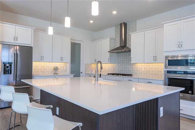 15600 Vetta Dr, Bella Collina, FL 34756 - kitchen featuring stainless steel appliances, wall chimney range hood, wood finished floors, a spacious island, and white cabinets