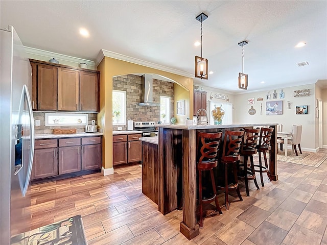 15311 Johns Lake Rd, Clermont, FL 34711 - kitchen featuring stainless steel appliances, crown molding, light countertops, wall chimney range hood, and a breakfast bar area