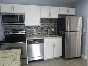5144 Picadilly Circus Ct Unit 2, Orlando, FL 32839 - kitchen featuring appliances with stainless steel finishes, white cabinets, decorative backsplash, and light stone counters
