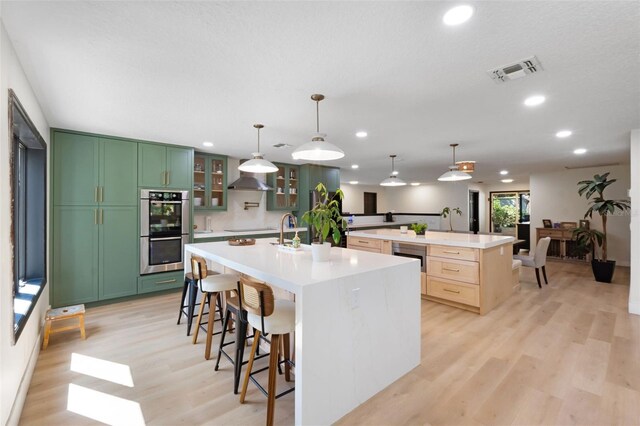 11951 Elbert St, Clermont, FL 34711 - kitchen with stainless steel double oven, a spacious island, light wood-type flooring, wall chimney range hood, and light countertops