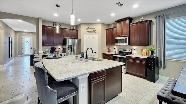 148 Whirlaway Dr, Davenport, FL 33837 - kitchen with stainless steel appliances, arched walkways, decorative light fixtures, light stone countertops, and a kitchen island with sink