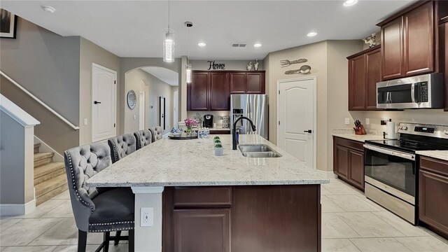 148 Whirlaway Dr, Davenport, FL 33837 - kitchen featuring appliances with stainless steel finishes, arched walkways, a kitchen bar, decorative light fixtures, and light stone counters