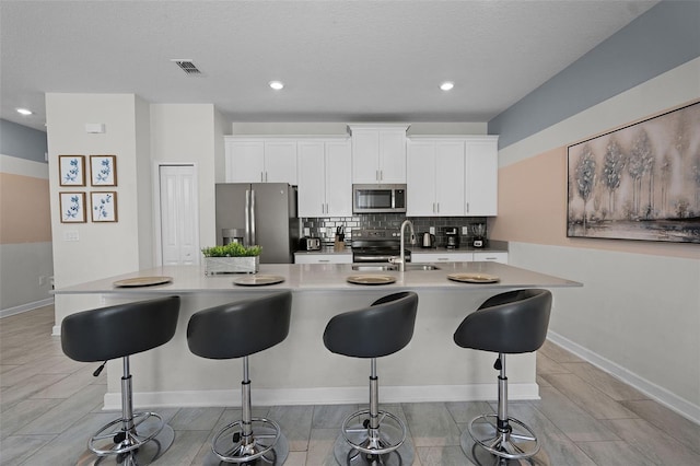 1565 Plunker Dr, Davenport, FL 33896 - kitchen with appliances with stainless steel finishes, a sink, tasteful backsplash, white cabinets, and a kitchen island with sink