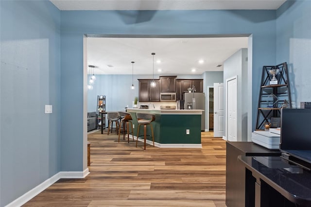 1064 Quaker Ridge Ln, Davenport, FL 33896 - kitchen featuring appliances with stainless steel finishes, light wood-style flooring, a breakfast bar, dark brown cabinetry, and light countertops