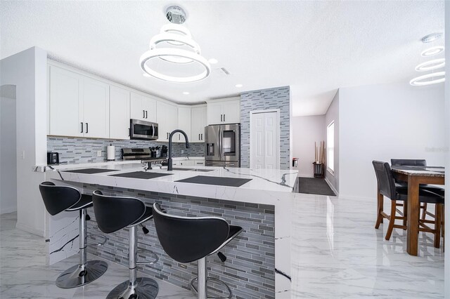 2503 Calla Lily Cv, Kissimmee, FL 34758 - kitchen with appliances with stainless steel finishes, a sink, light marble finish flooring, decorative backsplash, and a breakfast bar