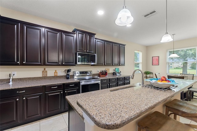 1353 Palmetto Dunes St, Davenport, FL 33836 - kitchen with stainless steel appliances, a kitchen bar, light stone counters, pendant lighting, and a kitchen island with sink