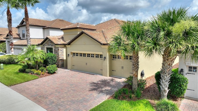 1353 Palmetto Dunes St, Davenport, FL 33836 - mediterranean / spanish-style house with stucco siding, decorative driveway, an attached garage, a tiled roof, and stone siding