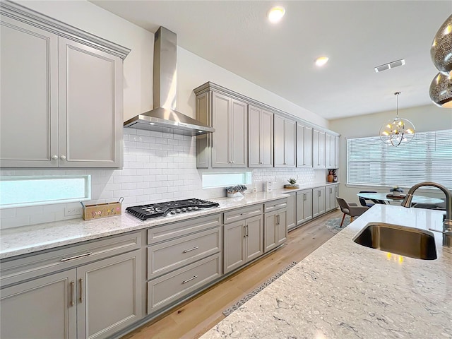 9071 Woodland Forest Rd, Orlando, FL 32836 - kitchen with wall chimney range hood, gray cabinets, stainless steel gas cooktop, backsplash, and light wood-style flooring