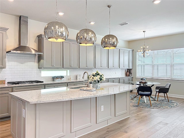 9071 Woodland Forest Rd, Orlando, FL 32836 - kitchen with wall chimney exhaust hood, gray cabinets, stainless steel gas cooktop, light wood-style floors, and backsplash