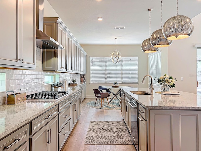 9071 Woodland Forest Rd, Orlando, FL 32836 - kitchen with wall chimney range hood, stainless steel gas stovetop, light wood finished floors, backsplash, and a chandelier