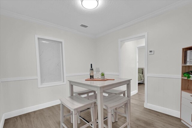 1501 Missouri Ave, Saint Cloud, FL 34769 - dining area with light wood-type flooring, crown molding, a textured ceiling, wainscoting, and a decorative wall