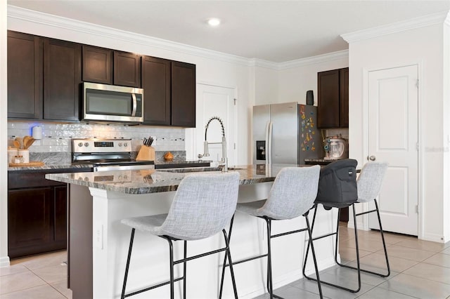 3255 Hilltop Cir, Bradenton, FL 34211 - kitchen with stainless steel appliances, dark brown cabinetry, light tile patterned floors, a center island with sink, and crown molding