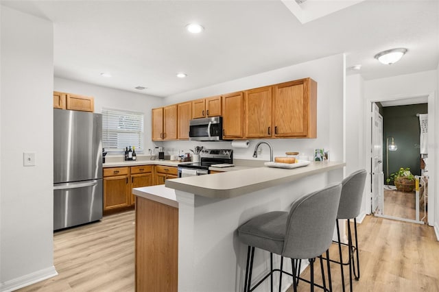 138 Hidden Pointe Ln, Groveland, FL 34736 - kitchen with appliances with stainless steel finishes, light wood-style floors, a breakfast bar area, a peninsula, and light countertops