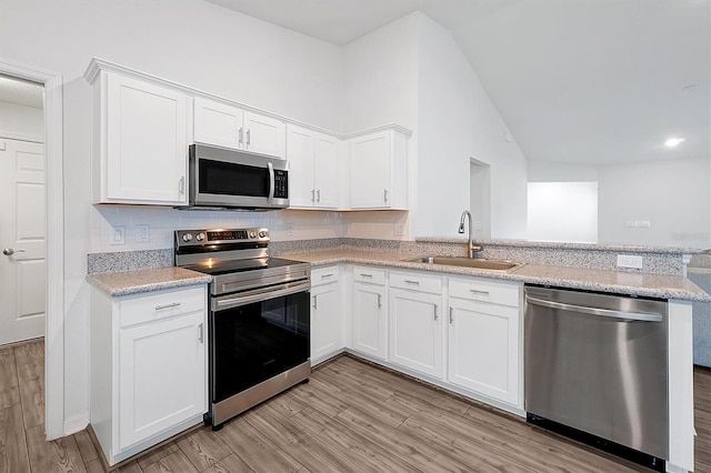 4505 Hummingbird Ln, Haines City, FL 33844 - kitchen with stainless steel appliances, a peninsula, light wood finished floors, lofted ceiling, and white cabinetry