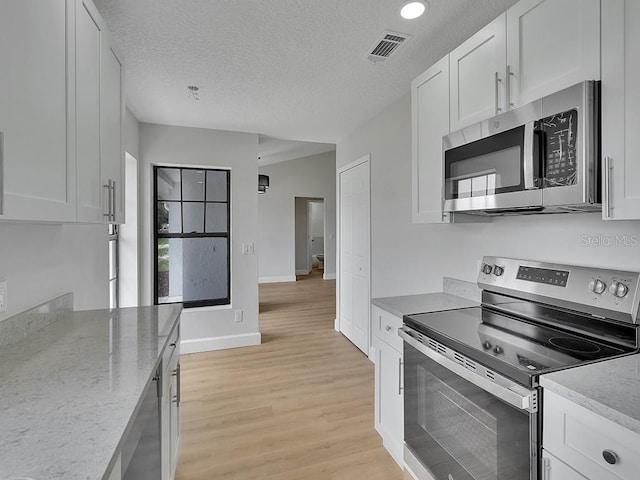 925 Roswell Ter, Deltona, FL 32738 - kitchen with stainless steel appliances, light wood-type flooring, white cabinetry, light stone counters, and a textured ceiling