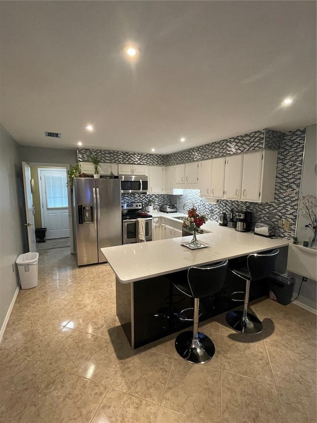 2013 Marilyn Ave, Winter Haven, FL 33881 - kitchen featuring appliances with stainless steel finishes, a peninsula, light countertops, decorative backsplash, and white cabinetry