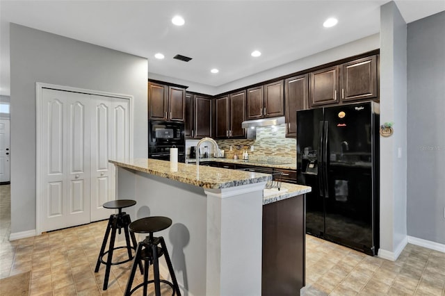 954 Revere Ave, Haines City, FL 33844 - kitchen with black appliances, under cabinet range hood, tasteful backsplash, dark brown cabinetry, and light stone countertops