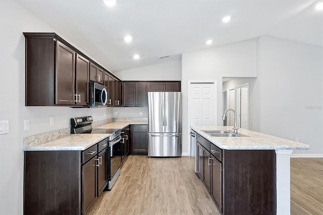 328 Lily Ln, Davenport, FL 33837 - kitchen with appliances with stainless steel finishes, vaulted ceiling, dark brown cabinets, light wood finished floors, and a kitchen island with sink