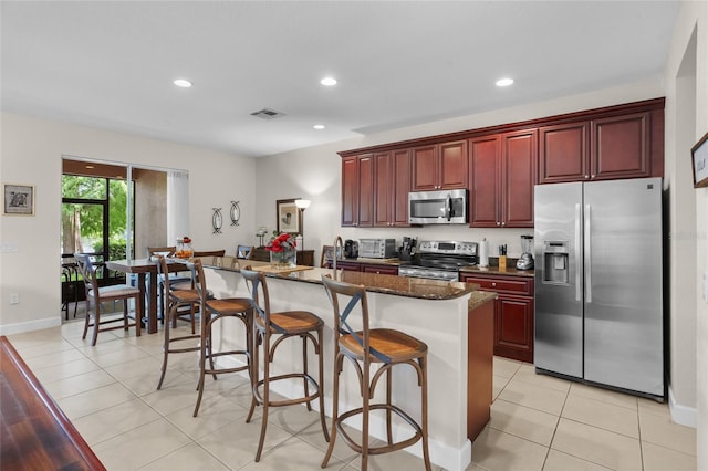 8401 Riverdale Ln Unit 8401, Davenport, FL 33896 - kitchen with stainless steel appliances, reddish brown cabinets, light tile patterned flooring, a kitchen island, and a kitchen bar