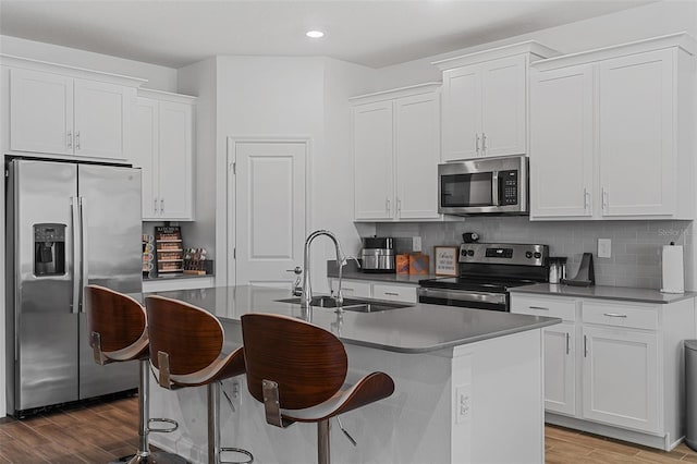 2759 Slash Way, Saint Cloud, FL 34771 - kitchen featuring appliances with stainless steel finishes, wood finished floors, a kitchen island with sink, white cabinets, and decorative backsplash