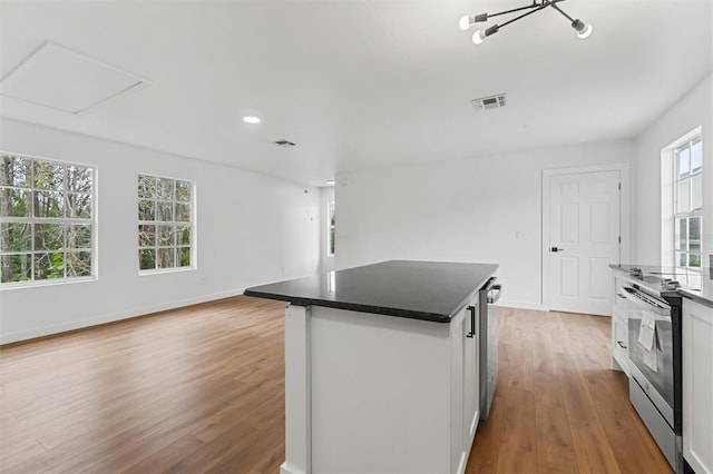 933 Jasmine St, Celebration, FL 34747 - kitchen with stainless steel electric range oven, light wood finished floors, dark countertops, a center island, and white cabinets