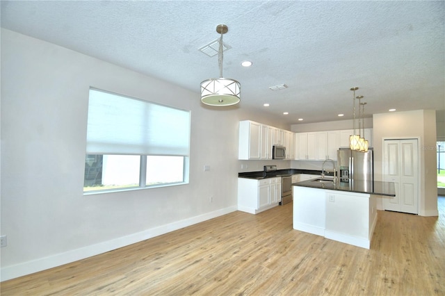 2673 Calistoga Ave, Kissimmee, FL 34741 - kitchen with stainless steel appliances, dark countertops, light wood-style floors, white cabinetry, and a textured ceiling