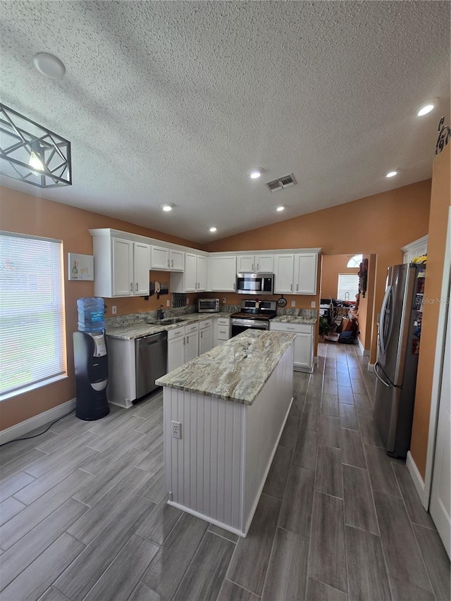 204 Canary Island Cir, Davenport, FL 33837 - kitchen with appliances with stainless steel finishes, wood finish floors, a center island, a textured ceiling, and white cabinets