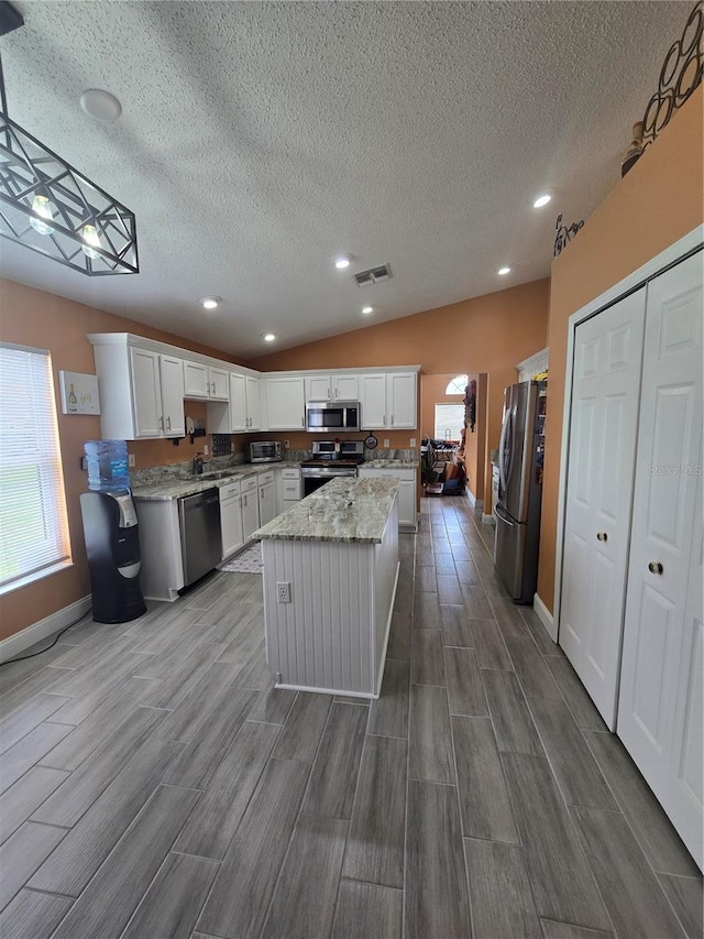 204 Canary Island Cir, Davenport, FL 33837 - kitchen featuring stainless steel appliances, wood tiled floors, a textured ceiling, a kitchen island, and light stone countertops