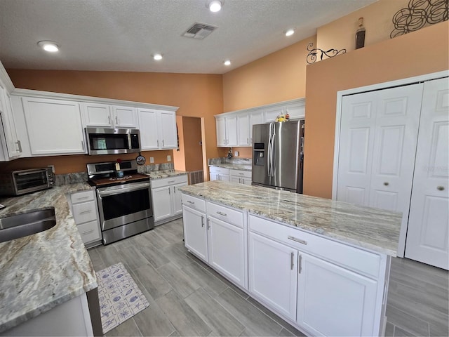 204 Canary Island Cir, Davenport, FL 33837 - kitchen featuring appliances with stainless steel finishes, vaulted ceiling, a kitchen island, white cabinetry, and a textured ceiling