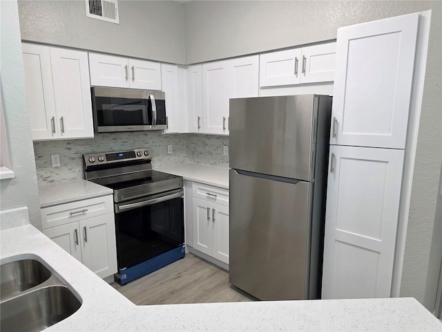 3428 Soho St Unit 208, Orlando, FL 32835 - kitchen with stainless steel appliances, white cabinetry, tasteful backsplash, light wood-style flooring, and light stone countertops