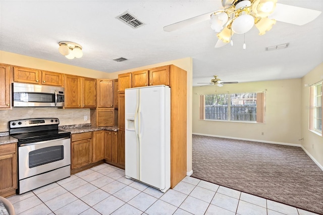 1101 Oregon Ave, Saint Cloud, FL 34769 - kitchen featuring stainless steel appliances, light colored carpet, ceiling fan, light tile patterned floors, and brown cabinets