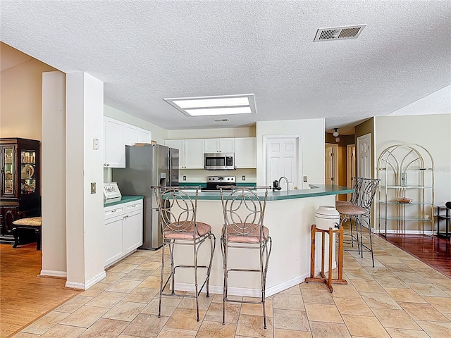 3158 Forest Breeze Way, Saint Cloud, FL 34771 - kitchen with appliances with stainless steel finishes, a breakfast bar area, white cabinets, a textured ceiling, and an island with sink