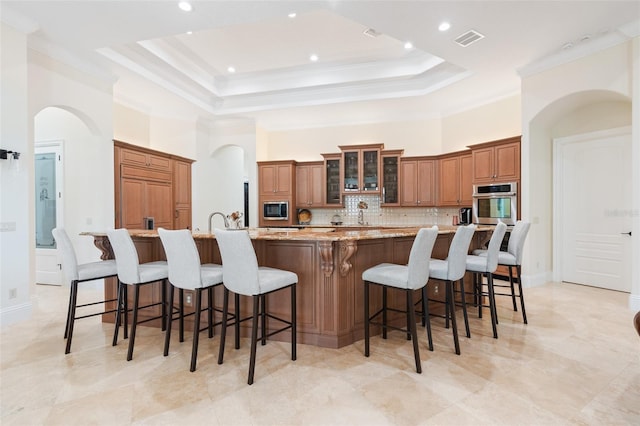 9905 Lanai View Ct, Windermere, FL 34786 - kitchen with appliances with stainless steel finishes, arched walkways, tasteful backsplash, brown cabinetry, and a towering ceiling