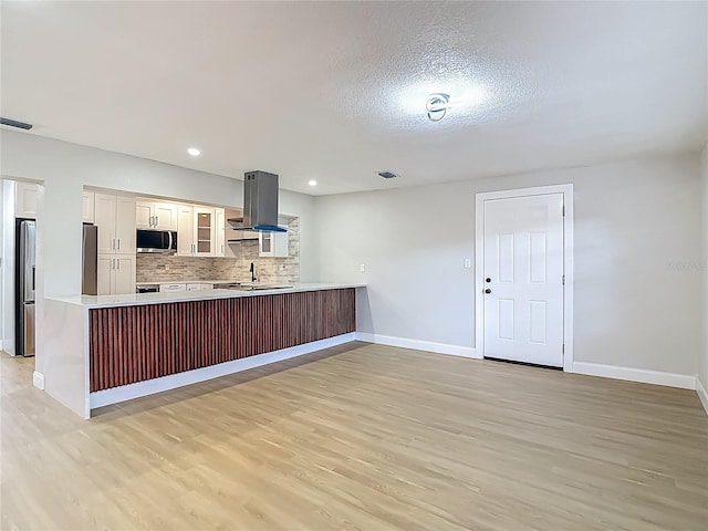 4202 W Bay Vista Ave, Tampa, FL 33611 - kitchen featuring appliances with stainless steel finishes, range hood, light wood-style flooring, a peninsula, and tasteful backsplash