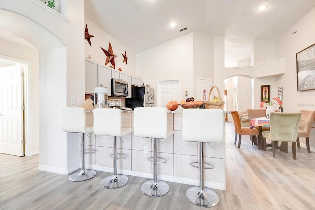 1014 Prey Ct, Kissimmee, FL 34746 - kitchen featuring stainless steel microwave, arched walkways, a breakfast bar, freestanding refrigerator, and high vaulted ceiling