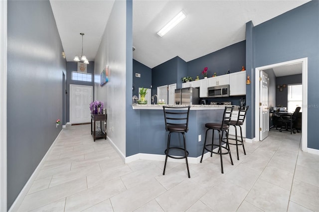 5100 Violet Ln, Kissimmee, FL 34758 - kitchen featuring appliances with stainless steel finishes, white cabinetry, a breakfast bar area, high vaulted ceiling, and light countertops