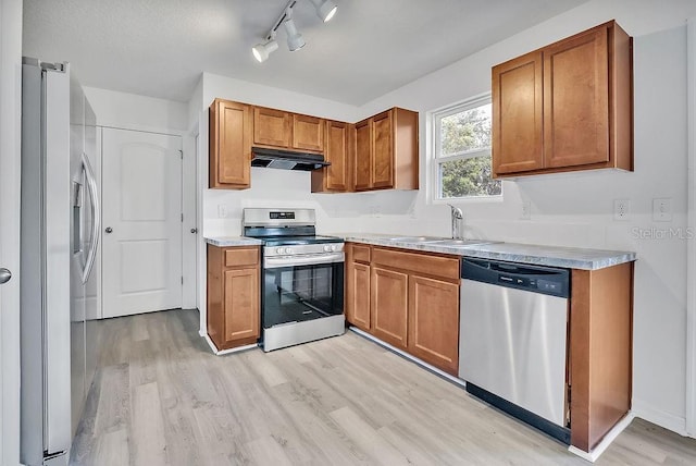 303 Anchovie Ct, Poinciana, FL 34759 - kitchen with stainless steel appliances, under cabinet range hood, light wood finished floors, brown cabinets, and light countertops