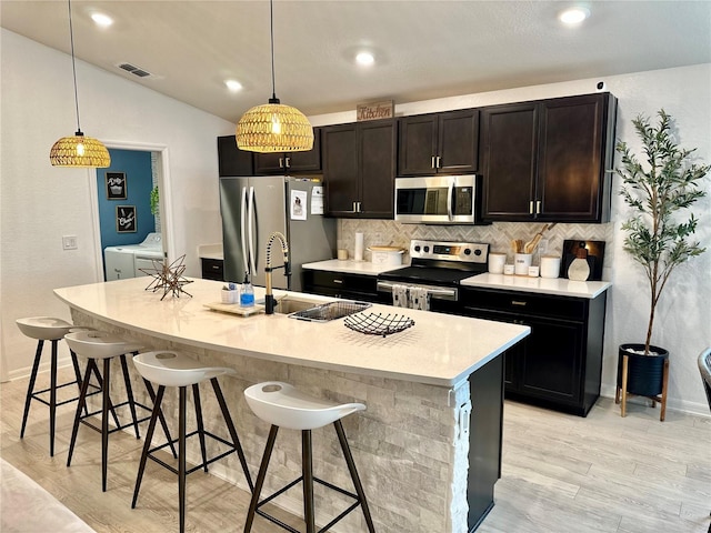 144 Foxtail Loop, Davenport, FL 33837 - kitchen with stainless steel appliances, washer and clothes dryer, decorative backsplash, light wood-style floors, and a breakfast bar area