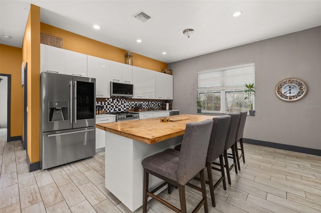 2576 R E Byrd Rd, Frostproof, FL 33843 - kitchen with stainless steel appliances, butcher block counters, a breakfast bar, white cabinetry, and decorative backsplash