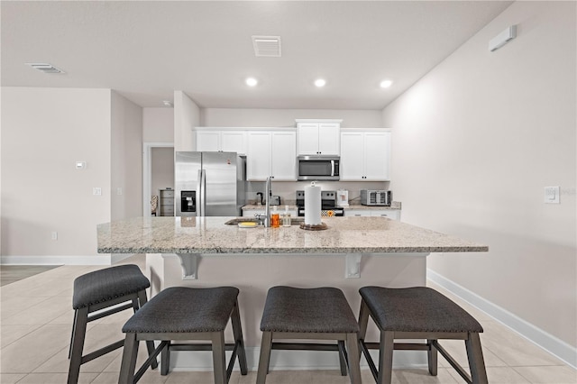 7413 Bent Tree Loop, Saint Cloud, FL 34771 - kitchen with appliances with stainless steel finishes, an island with sink, white cabinets, light stone countertops, and a breakfast bar area