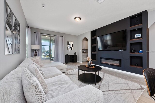 11051 Bostwick Aly, Winter Garden, FL 34787 - living area featuring arched walkways, light wood-style floors, a glass covered fireplace, and built in features