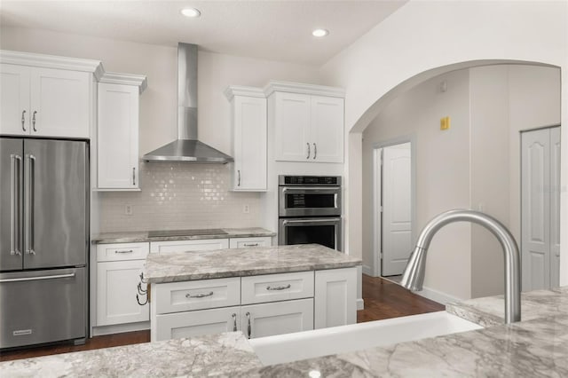 502 Mirasol Cir Unit 103, Kissimmee, FL 34747 - kitchen featuring appliances with stainless steel finishes, wall chimney exhaust hood, white cabinetry, arched walkways, and light stone counters