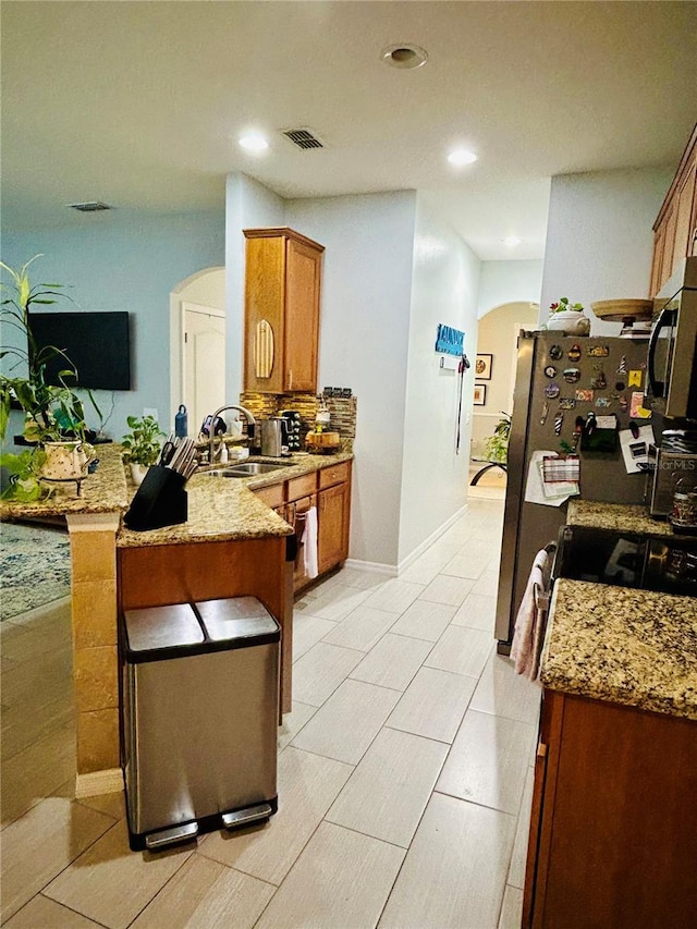 2862 Grasmere View Pkwy, Kissimmee, FL 34746 - kitchen with arched walkways, stainless steel microwave, brown cabinetry, a peninsula, and recessed lighting