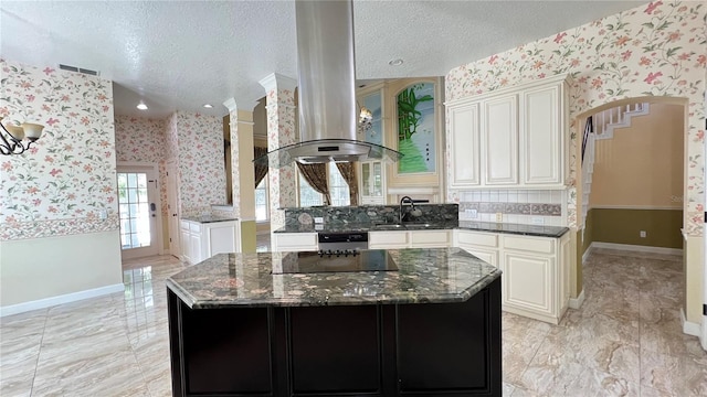 934 Westpark Dr, Celebration, FL 34747 - kitchen with wallpapered walls, island exhaust hood, dark stone counters, decorative columns, and a kitchen island