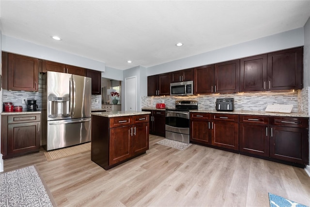 13129 Cog Hill Way, Orlando, FL 32828 - kitchen with appliances with stainless steel finishes, decorative backsplash, light wood-type flooring, a center island, and light stone countertops