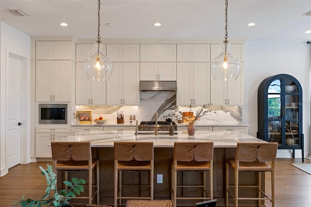 9352 Santorini Dr, Orlando, FL 32827 - kitchen with stainless steel microwave, under cabinet range hood, backsplash, wood finished floors, and light stone countertops