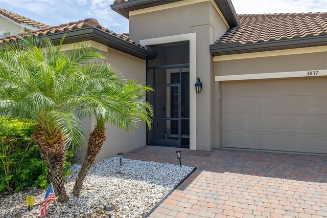 3837 Carrick Bend Dr, Kissimmee, FL 34746 - doorway to property featuring stucco siding, a tile roof, decorative driveway, and an attached garage