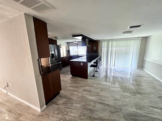 12215 Cobble Stone Dr, Hudson, FL 34667 - kitchen featuring a breakfast bar area, a peninsula, a textured ceiling, dark brown cabinetry, and dark countertops