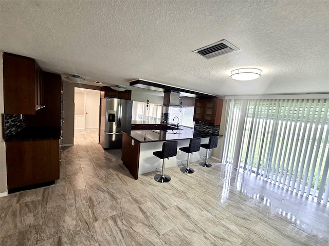 12215 Cobble Stone Dr, Hudson, FL 34667 - kitchen with stainless steel fridge with ice dispenser, a breakfast bar area, dark countertops, a peninsula, and a textured ceiling